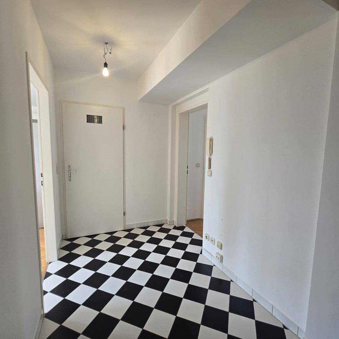 Heller Flur mit markantem schwarz-weißem Schachbrettmuster-Fliesenboden und weißen Wänden.
