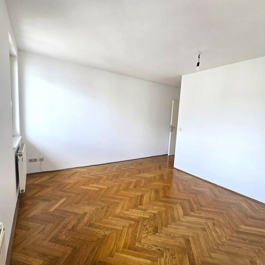 Helles Zimmer mit Fischgrätparkettboden und weißen Wänden, bereit zur individuellen Gestaltung.