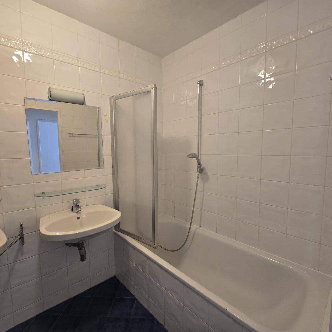 Gefliestes Badezimmer mit Badewanne, Duschabtrennung und einem einzelnen Waschbecken.