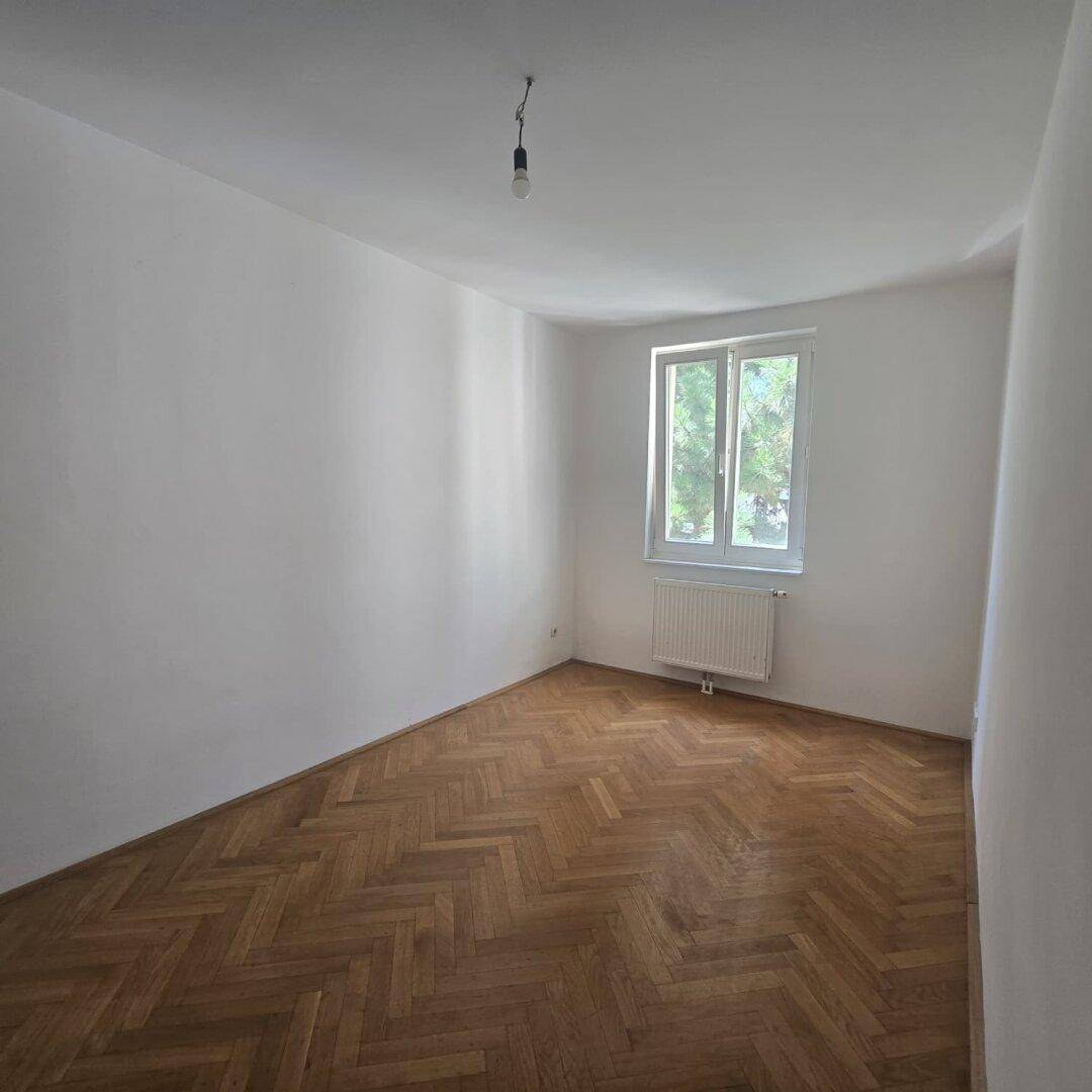 Ruhiges Schlafzimmer mit Fischgrätparkett und einem Fenster, das viel Tageslicht hereinlässt.