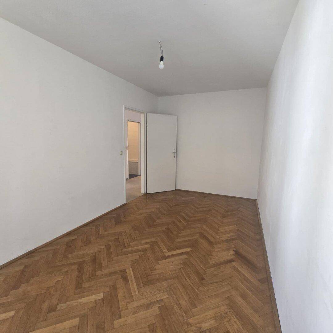 Geräumiges Schlafzimmer mit elegantem Fischgrätparkett und weiß gestrichenen Wänden.
