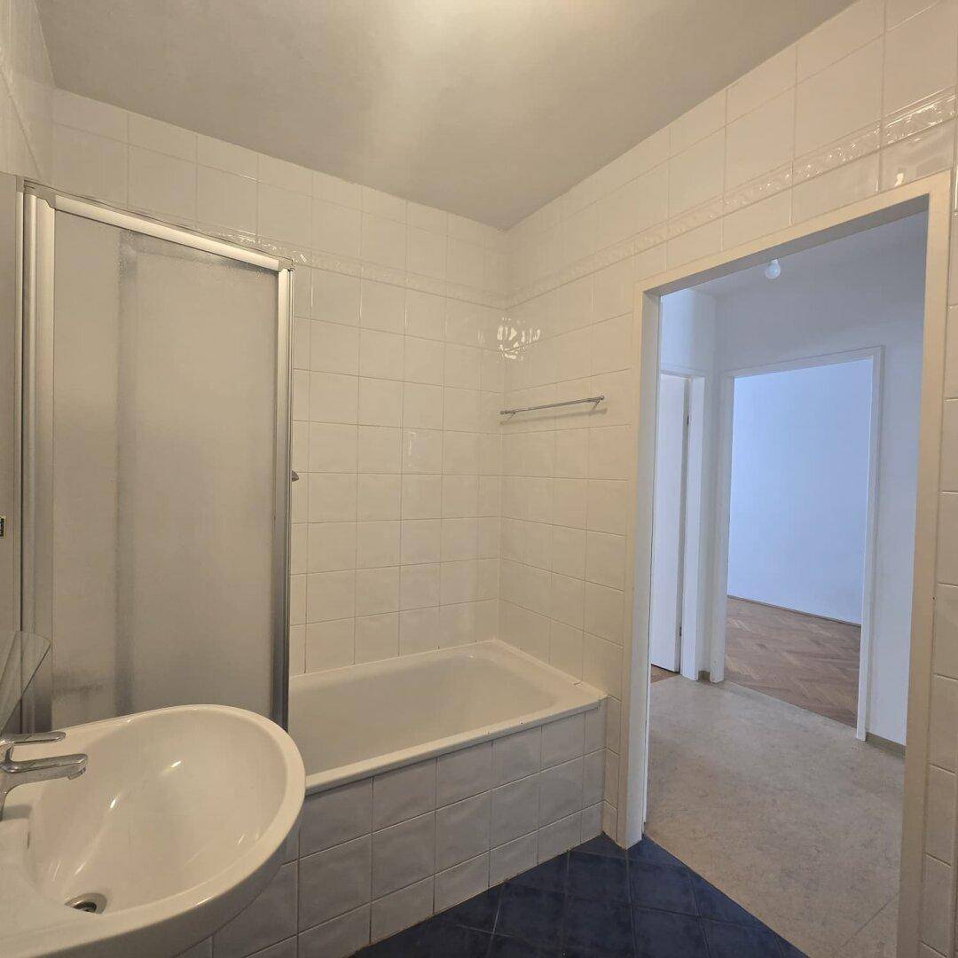 Funktionales Badezimmer mit Badewanne, Duschabtrennung und einem Waschbecken, hell gefliest.