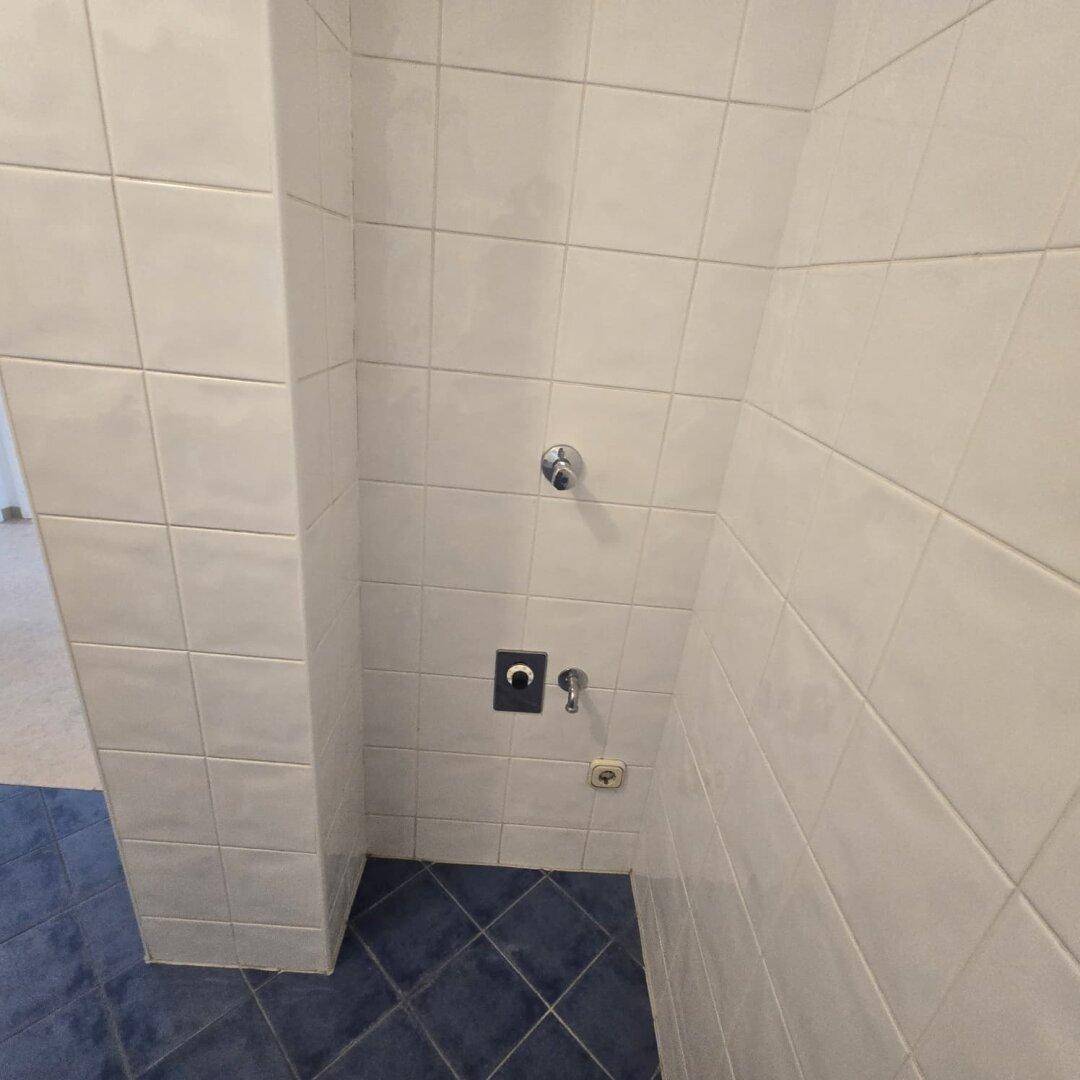 Ecke eines Badezimmers oder Hauswirtschaftsraums mit Fliesen und Anschlüssen.