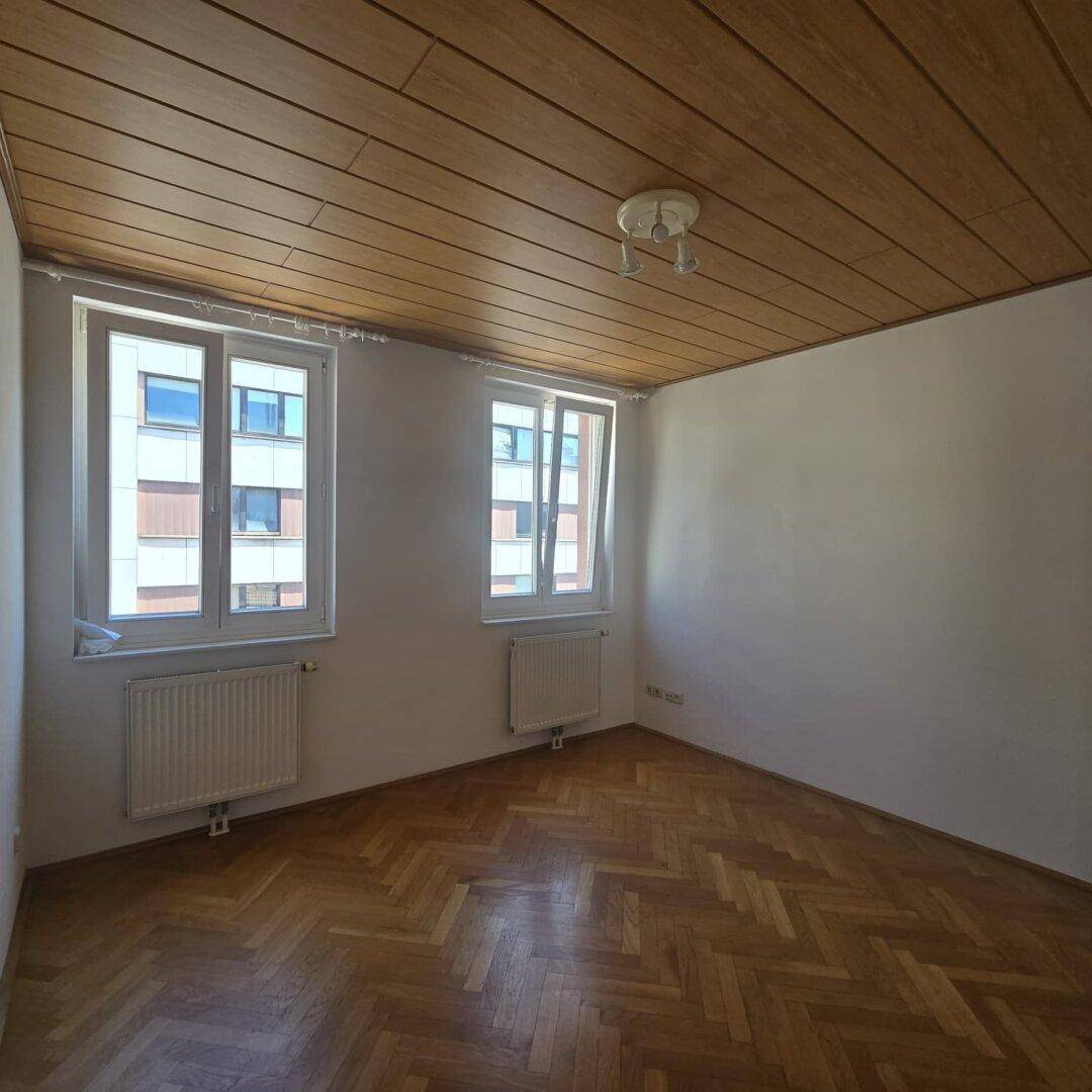 Helles Schlafzimmer mit Fischgrätparkett, Holzdecke und zwei Fenstern für viel Tageslicht.