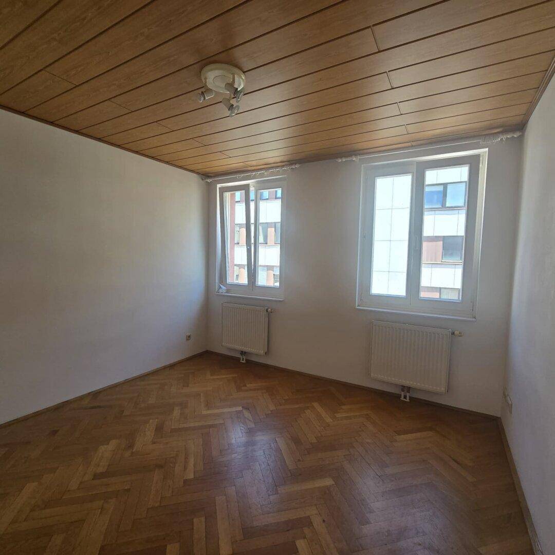 Gemütliches Schlafzimmer mit Fischgrätparkett und einer warmen Holzdecke, gut belichtet.