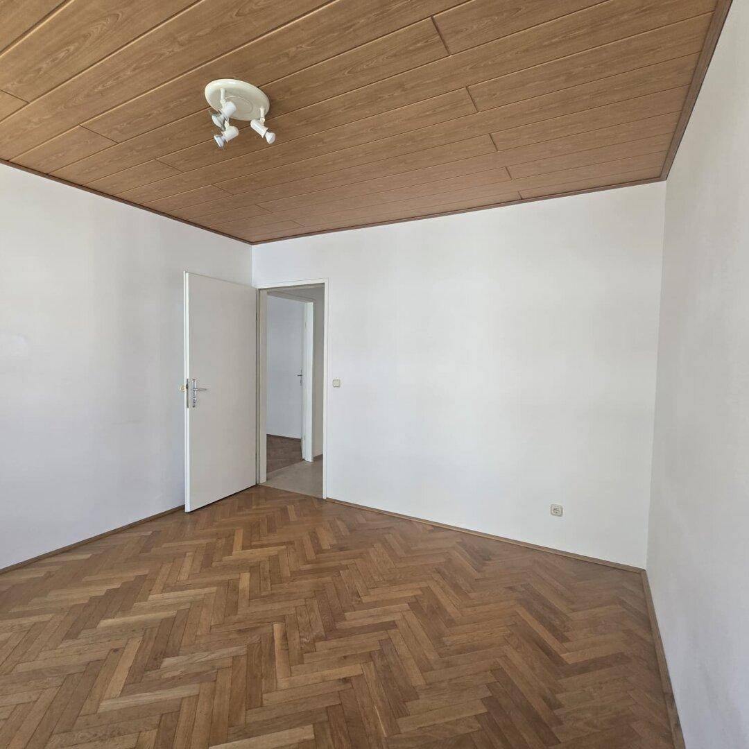 Schlafzimmer mit klassischem Fischgrätparkett und einer charakteristischen Holzdecke.