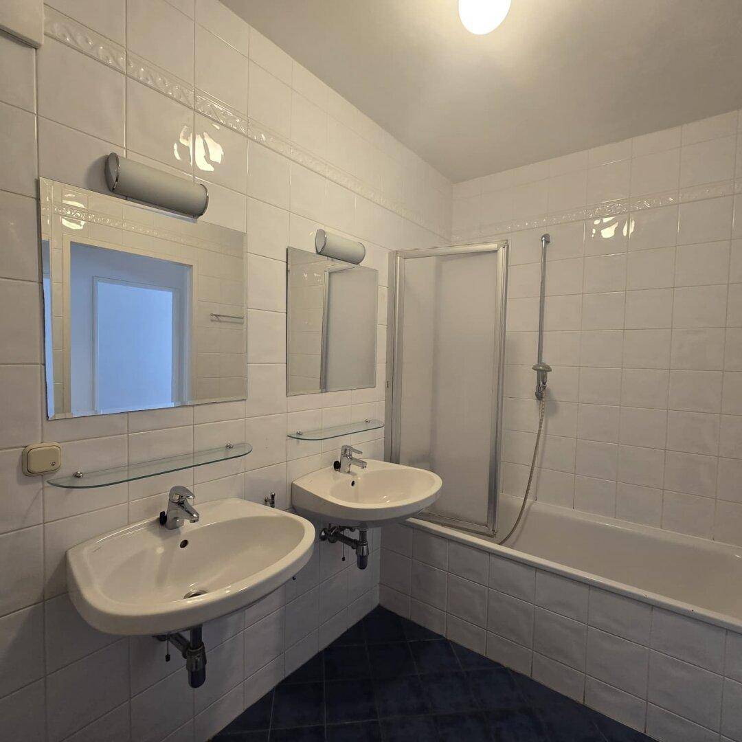 Badezimmer mit zwei Waschbecken, Badewanne mit Duschabtrennung und weißen Wandfliesen.
