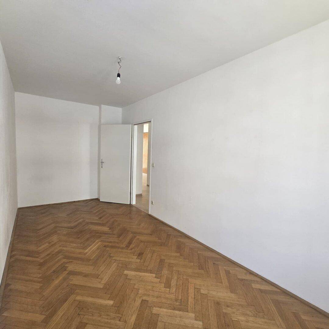 Geräumiges Wohnzimmer mit Fischgrätparkett und hellen Wänden, bereit zur individuellen Gestaltung.