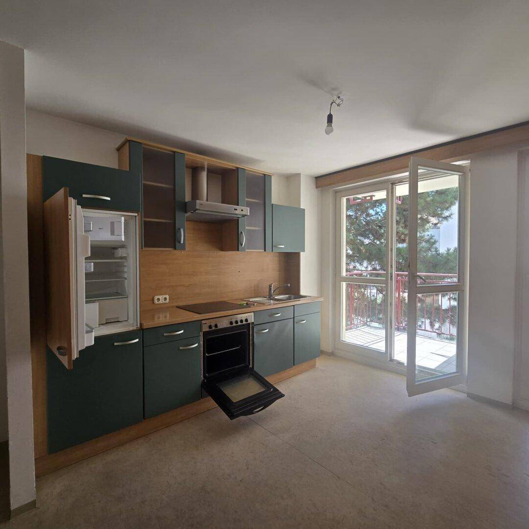 Funktionale Küche mit geöffnetem Kühlschrank und Balkonzugang, hell und praktisch.