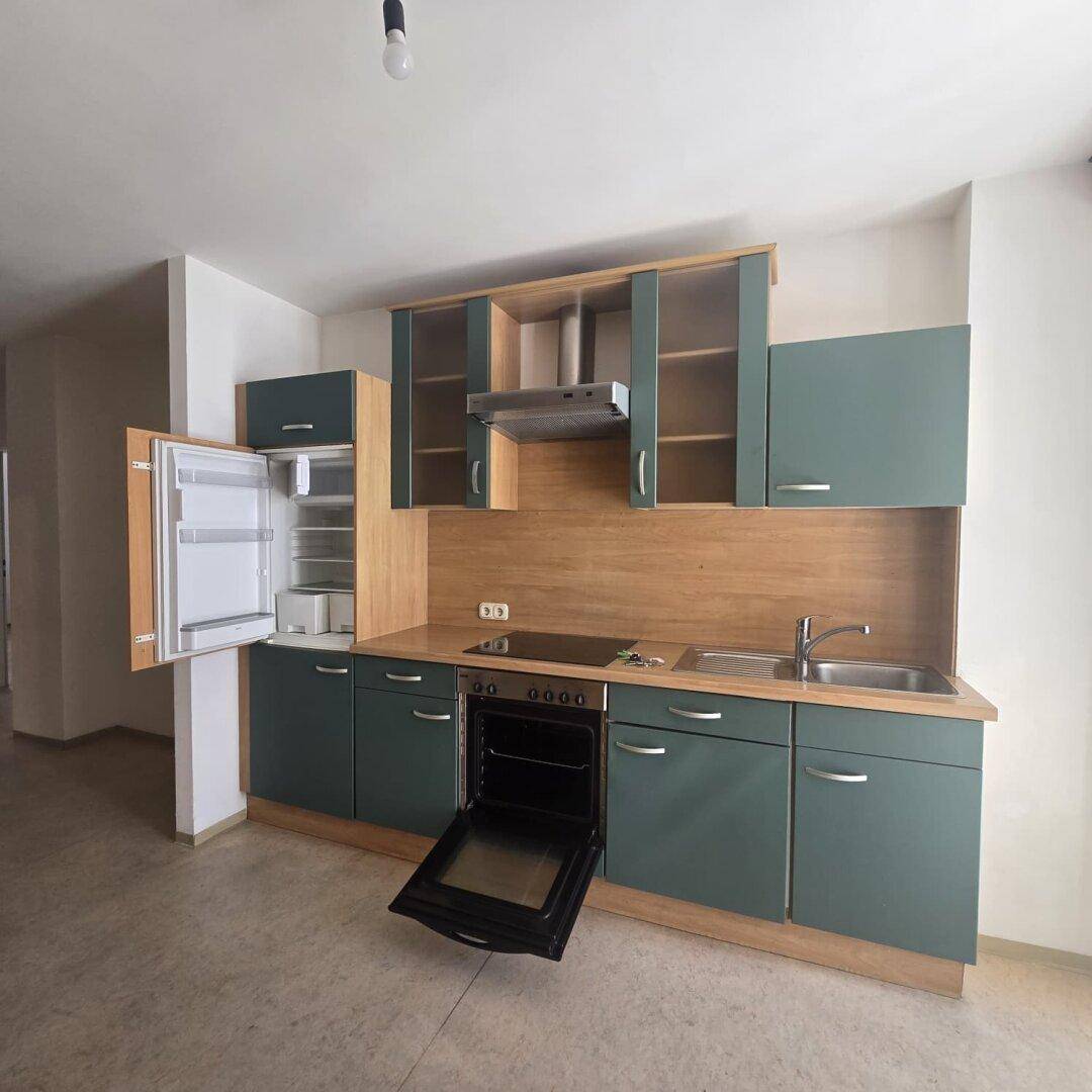 Gut ausgestattete Einbauküche mit Kühlschrank, Backofen und Kochfeld, in Grün und Holz.