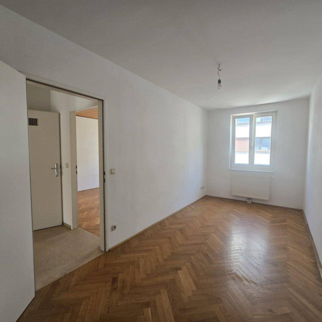 Helles Schlafzimmer mit klassischem Fischgrätparkett und weiß gestrichenen Wänden.