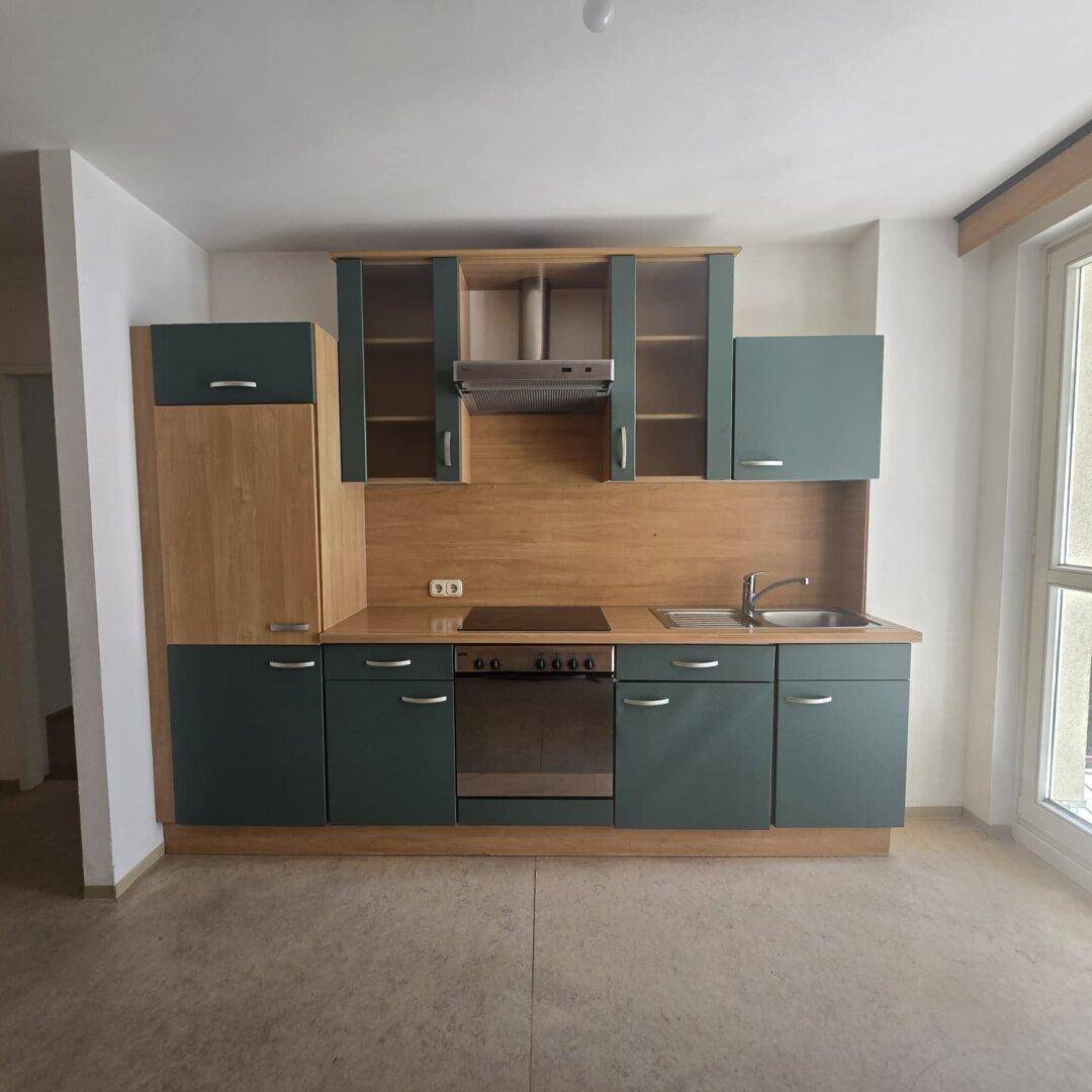 Moderne Einbauküche mit grünen und holzfarbenen Schränken, ausgestattet mit Herd und Spüle.