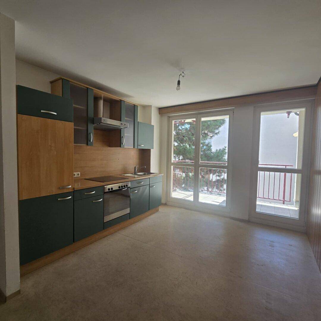 Funktionale Einbauküche mit grünen und holzfarbenen Fronten, direktem Zugang zum Balkon.