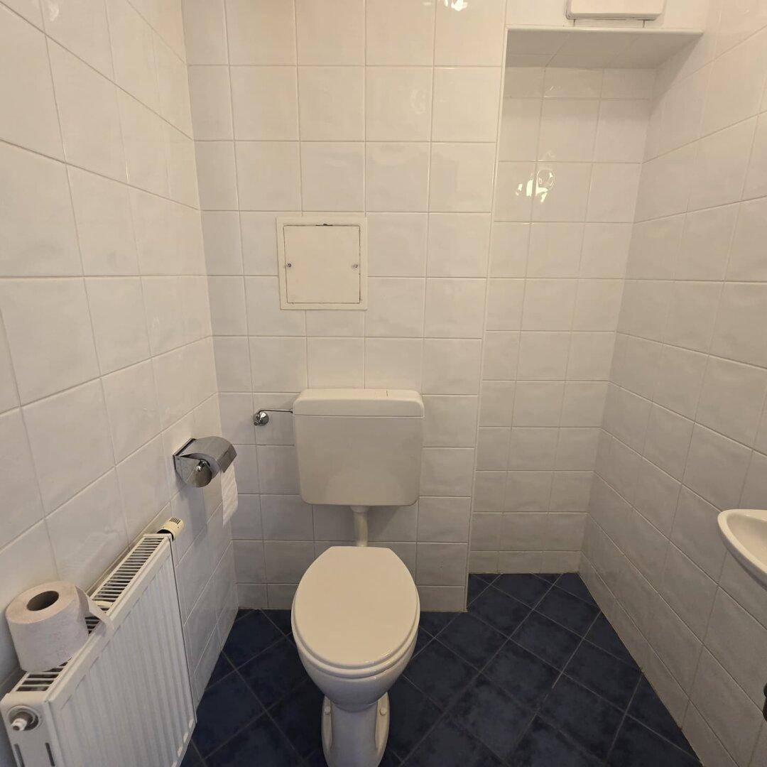 Kleines Gäste-WC mit weißen Fliesen, Toilette und Handwaschbecken, funktional gestaltet.