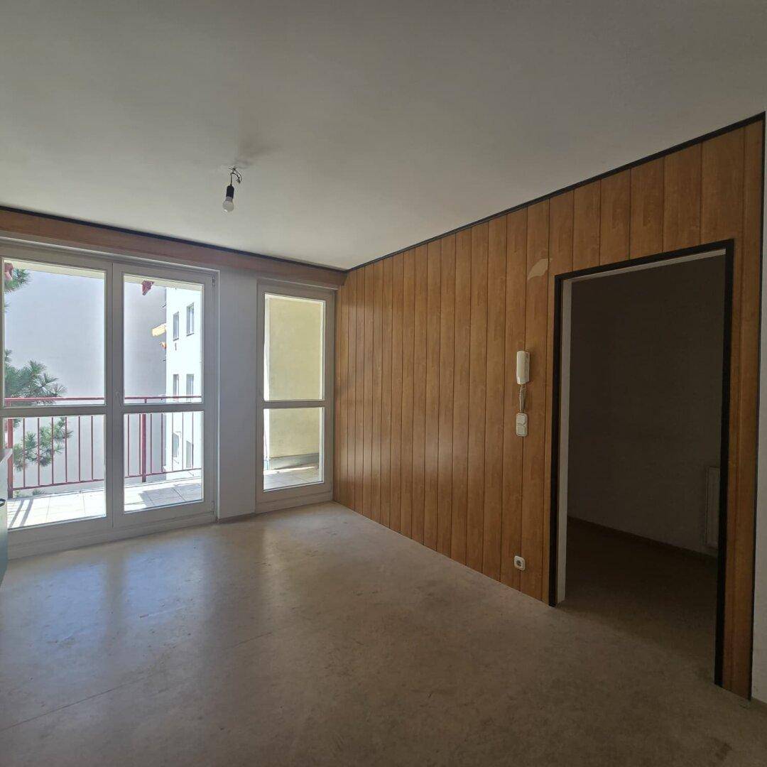 Heller Wohnbereich mit Holzvertäfelung und großem Fenster mit Zugang zum Balkon.