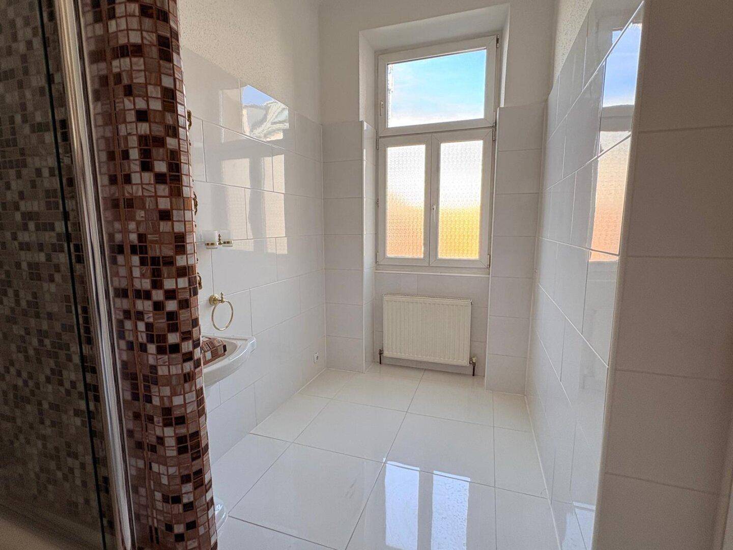 Helles Badezimmer mit weißen Fliesen, Fenster und Heizkörper.