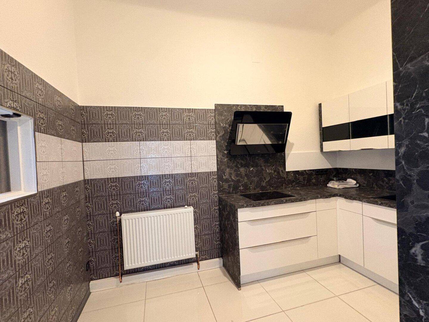 Moderne Küche mit weißen Hochglanzschränken, dunkler Arbeitsplatte und Fliesenboden.