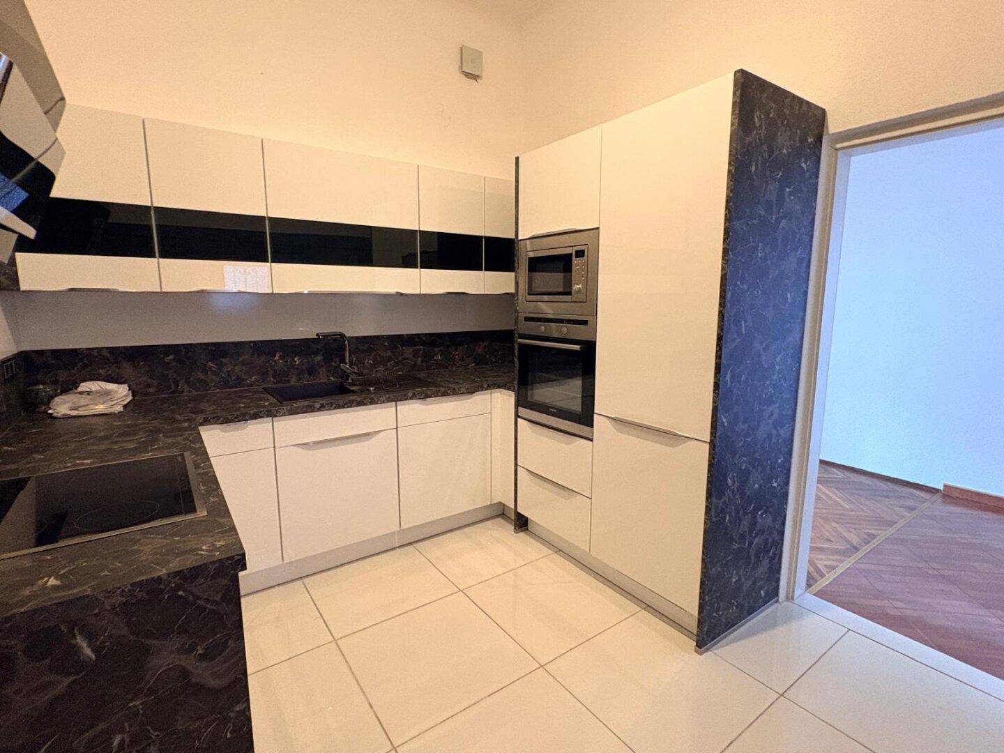 Voll ausgestattete Küche mit weißen Schränken, dunkler Arbeitsplatte und Einbaugeräten.