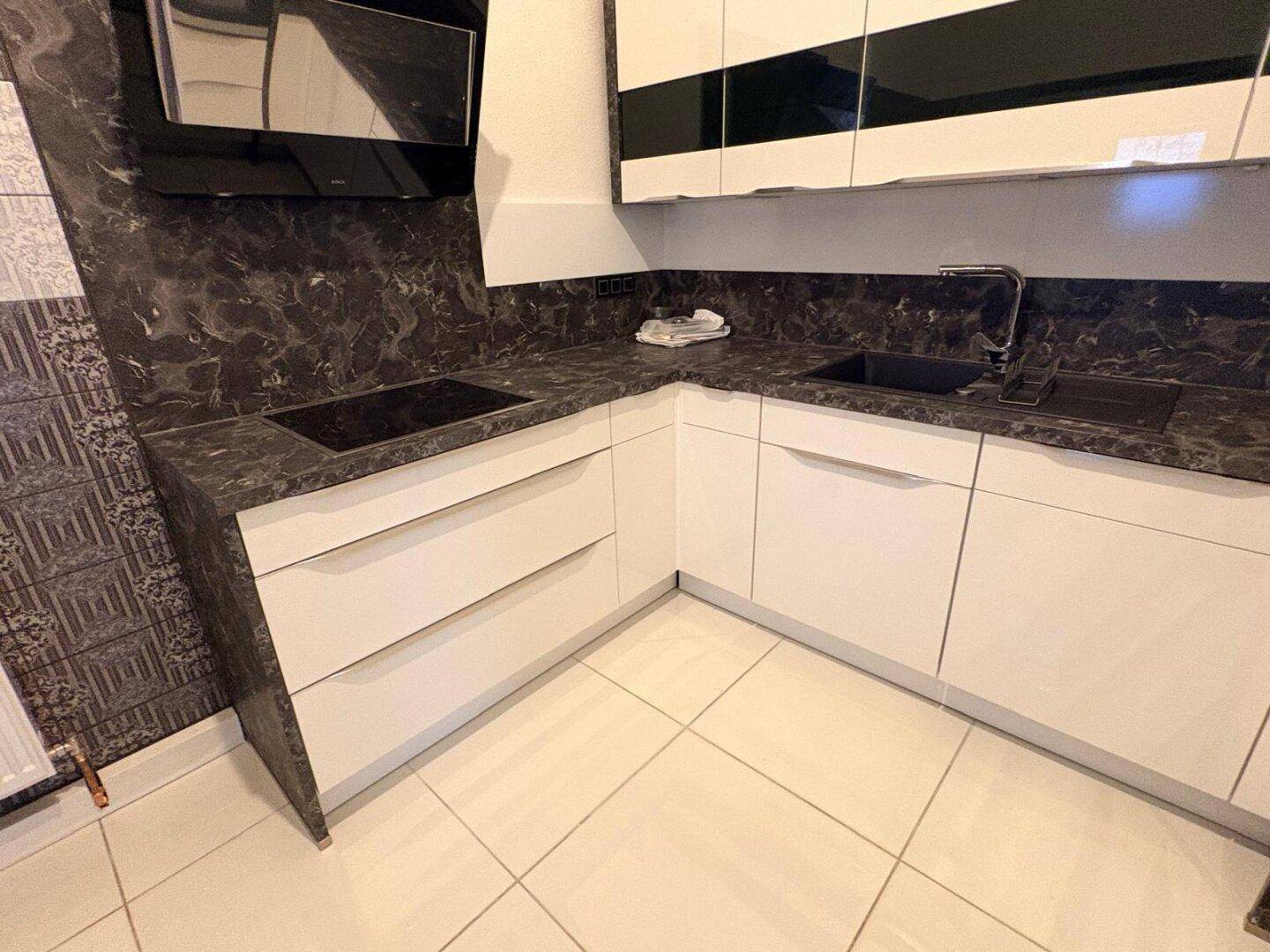 Moderne Einbauküche mit weißen Fronten, dunkler Arbeitsplatte und Spülbecken.