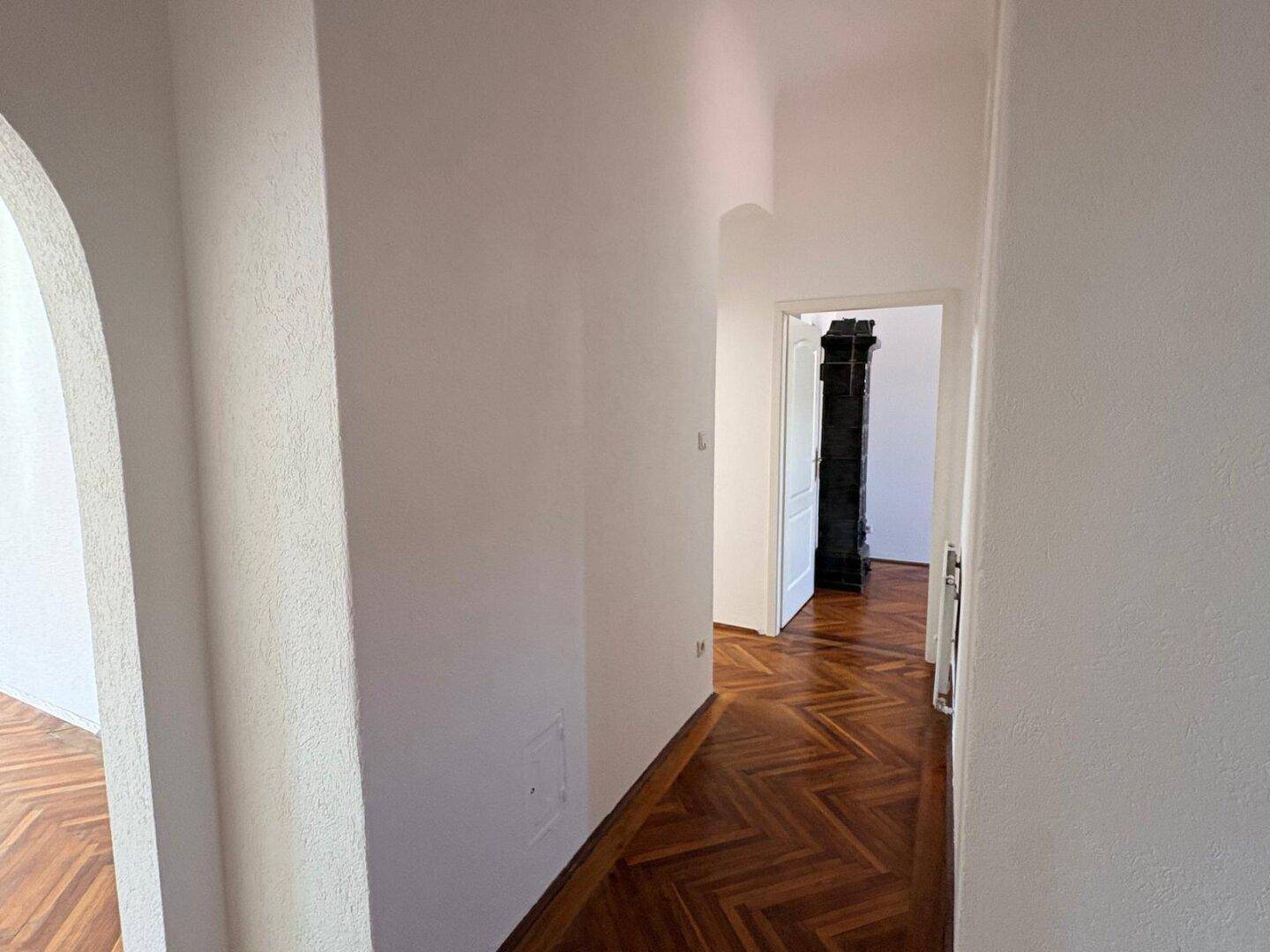 Langer Flur mit Fischgrätparkett und einem eleganten Bogen zum nächsten Raum.