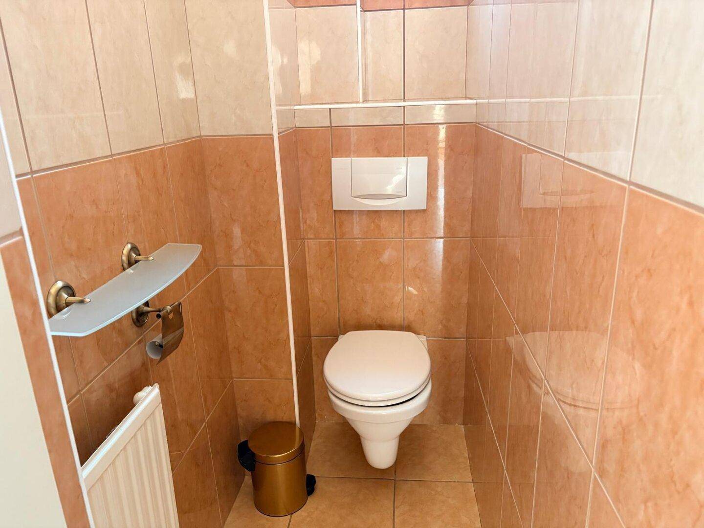 Kleines WC mit beigefarbenen Fliesen und wandhängender Toilette.
