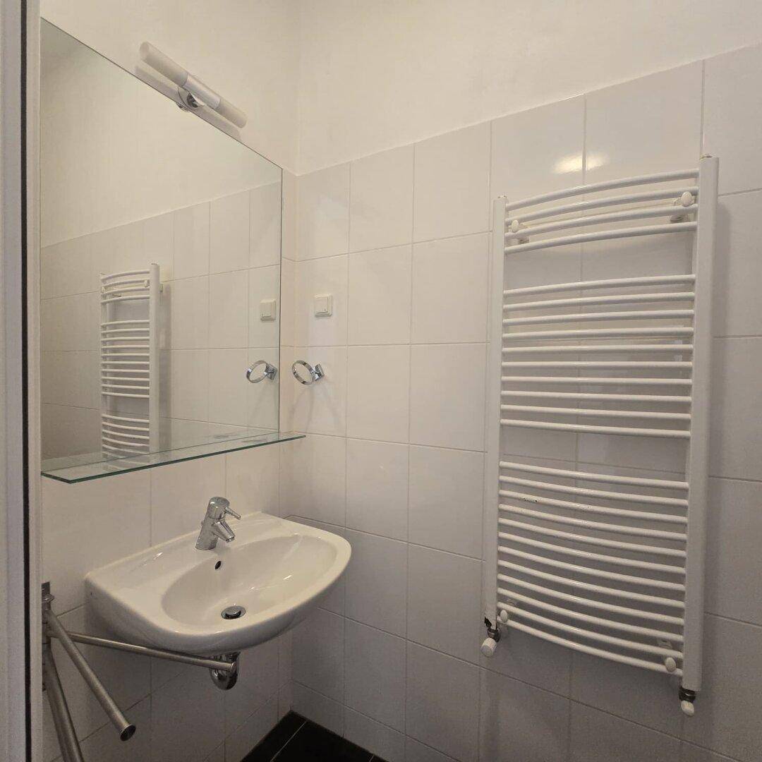 Modernes Badezimmer mit weißem Waschbecken, Spiegel und beheiztem Handtuchhalter.