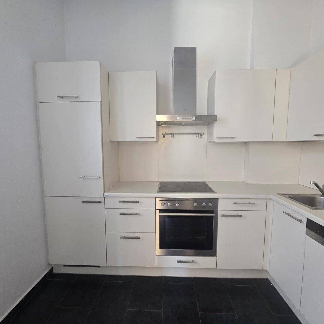 Moderne Einbauküche mit weißen Schränken, Kochfeld, Backofen und Dunstabzugshaube.