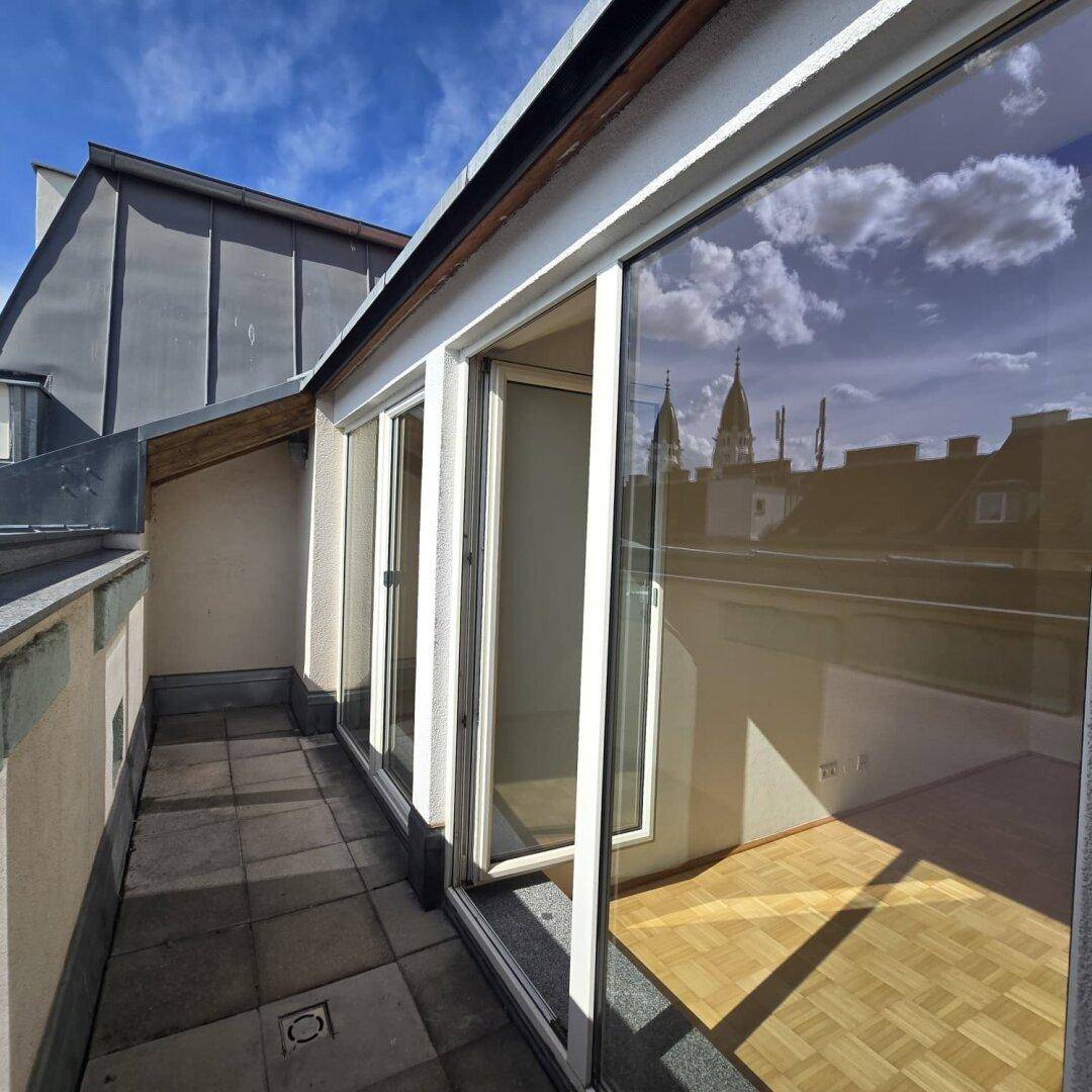 Schmaler Balkon mit Fliesenboden und großen Glasfronten, die den Blick auf die Stadt freigeben.
