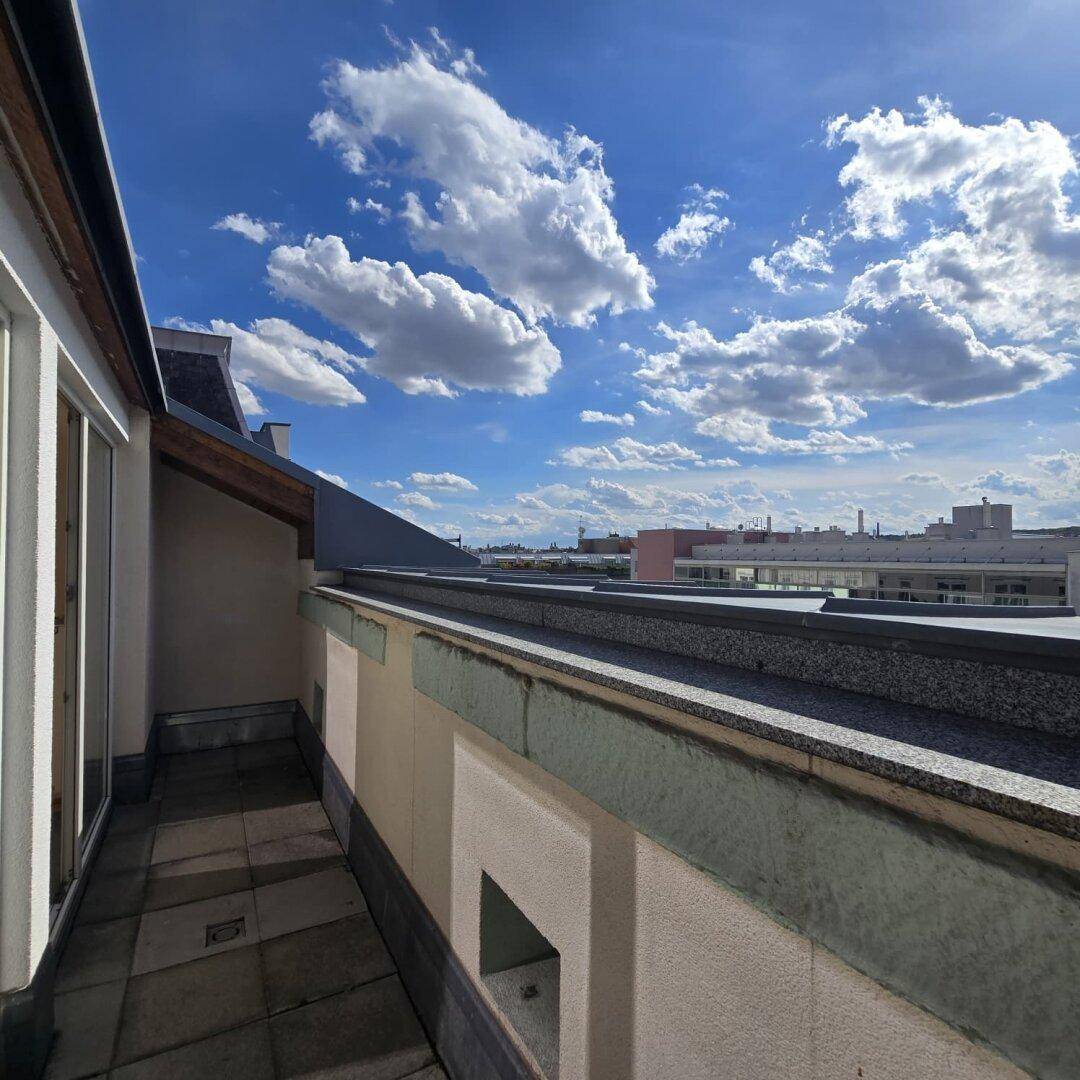 Langer Balkon mit Fliesenboden und Blick auf die umliegende Stadtlandschaft und Dächer.