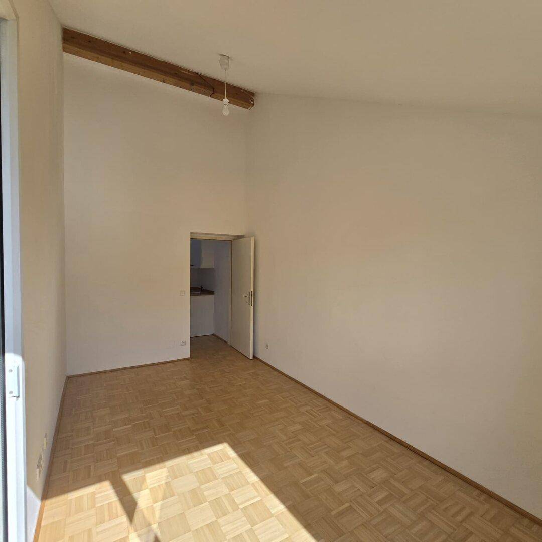 Geräumiger Wohnbereich mit Holzbalken an der Decke und Zugang zu weiteren Räumen.