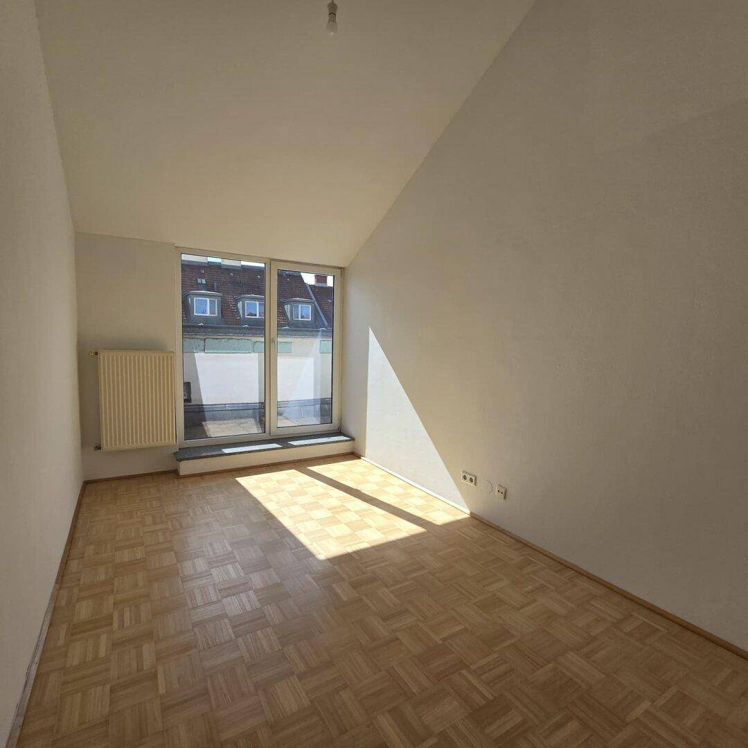 Lichtdurchfluteter Raum mit Parkettboden, schrägen Wänden und einem großen Fenster für viel Tageslicht.