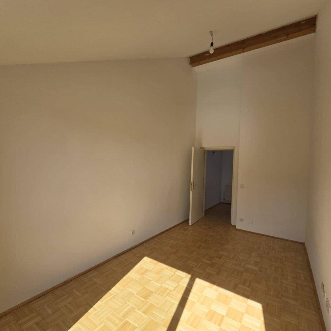 Geräumiger Wohnbereich mit Holzbalken an der Decke und Zugang zu weiteren Räumen.