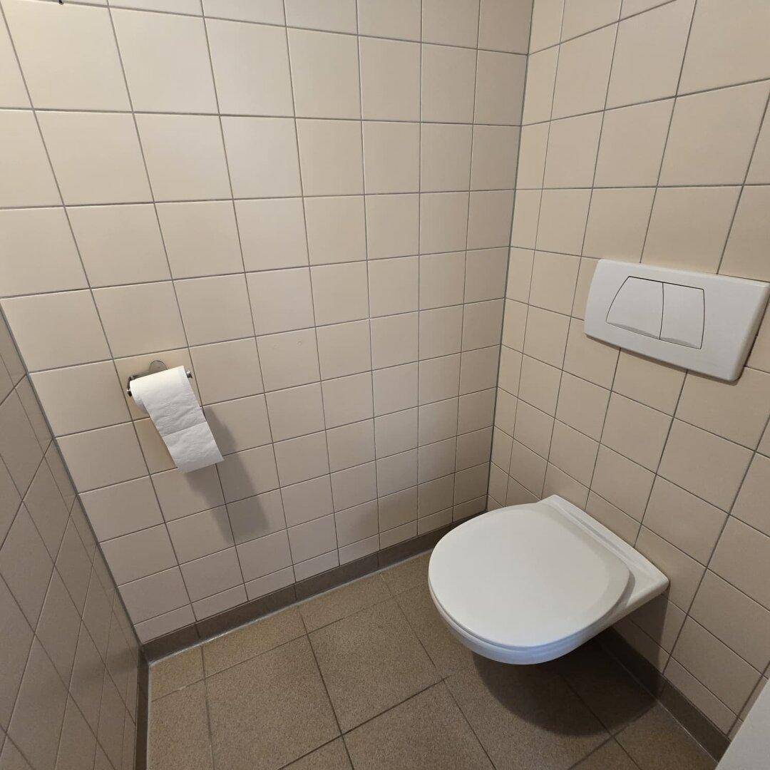 Separates WC mit beigefarbenen Wandfliesen und wandhängender Toilette.