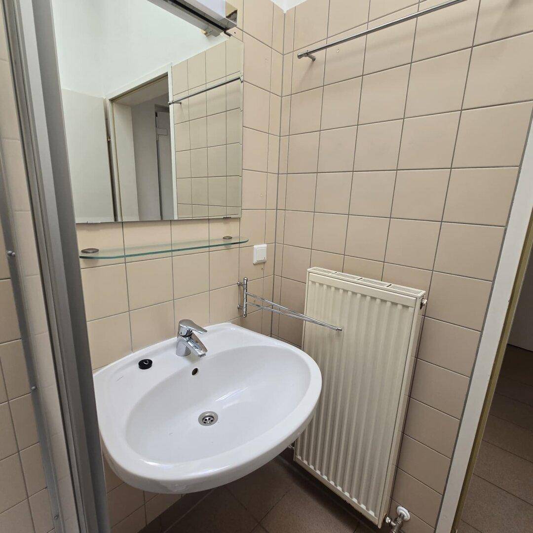 Badezimmer mit Waschbecken, Spiegel und Heizkörper, passend zu den beigefarbenen Wandfliesen.