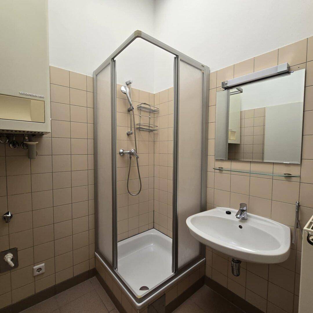 Badezimmer mit beigefarbenen Fliesen, Eckdusche und Waschbecken, in gutem Zustand.