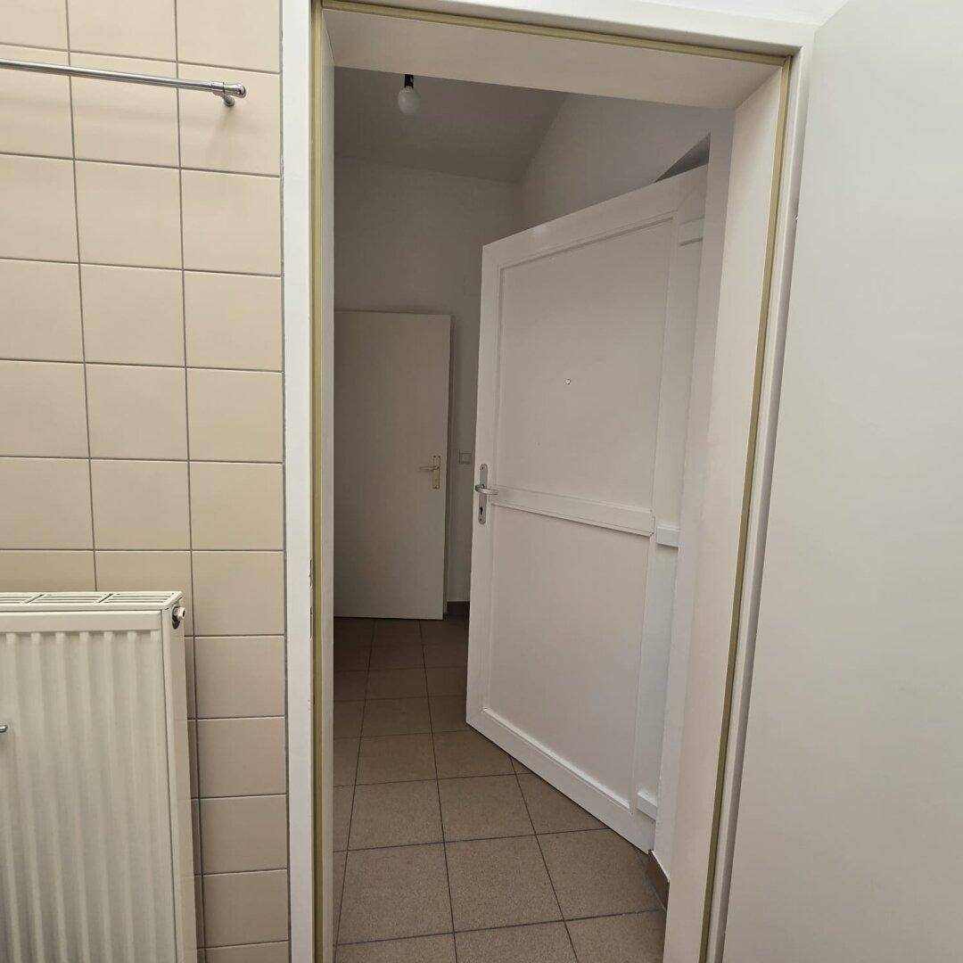 Blick vom Badezimmer in den Flur mit Fliesenboden und weißer Tür.