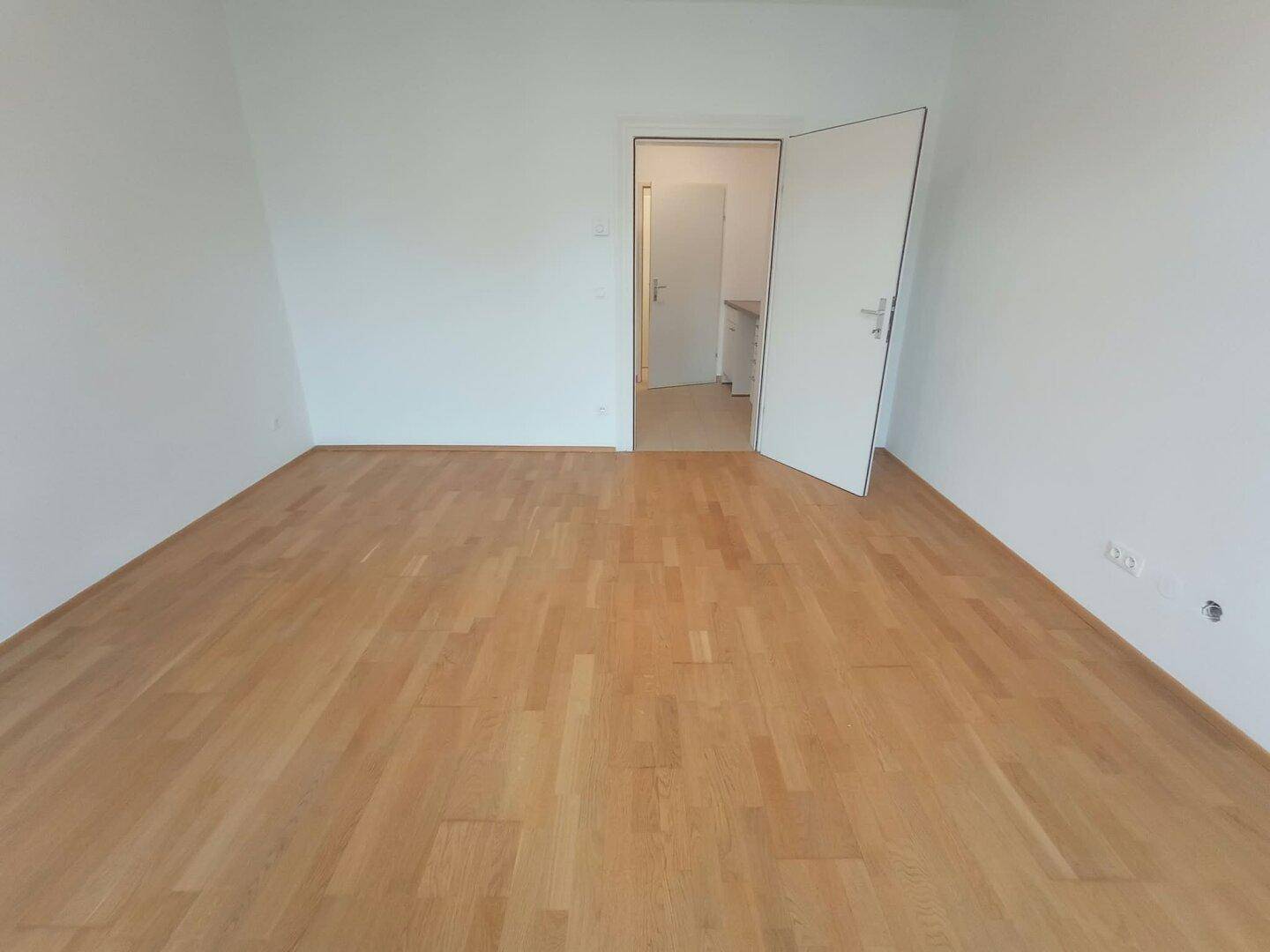 Geräumiges Zimmer mit Parkettboden und Zugang zu einem weiteren Raum.