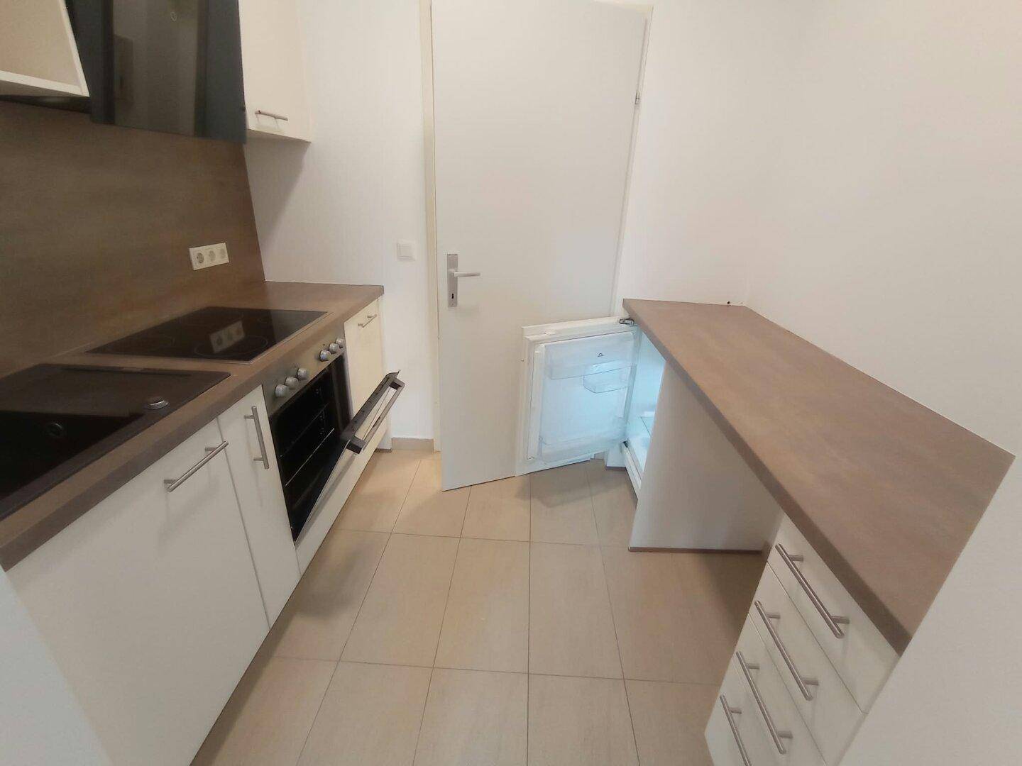 Kompakte Küche mit integriertem Kühlschrank, Kochfeld und praktischer Arbeitsfläche.