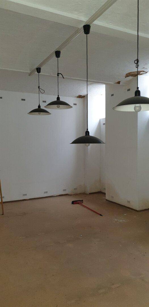 Leerer Raum mit schlichten Pendelleuchten und einfacher Deckenkonstruktion.