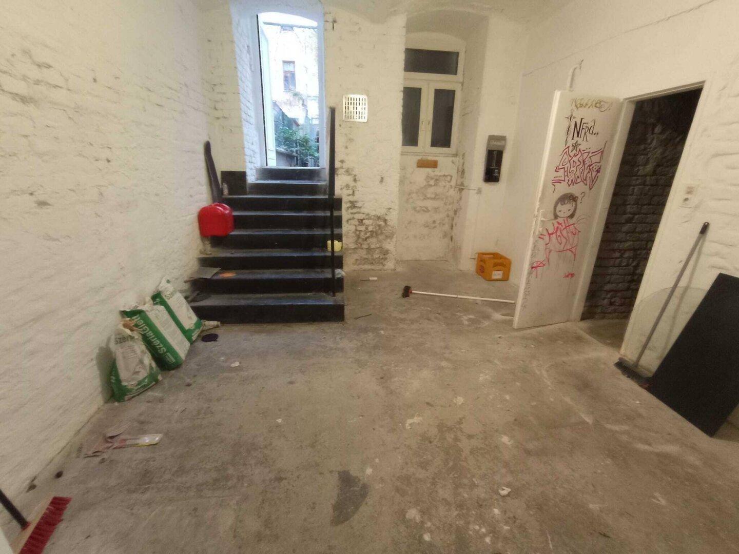 Kellerraum mit Treppe zum Ausgang, unverputzten Wänden und einem kleinen Fenster, das Tageslicht hereinlässt.
