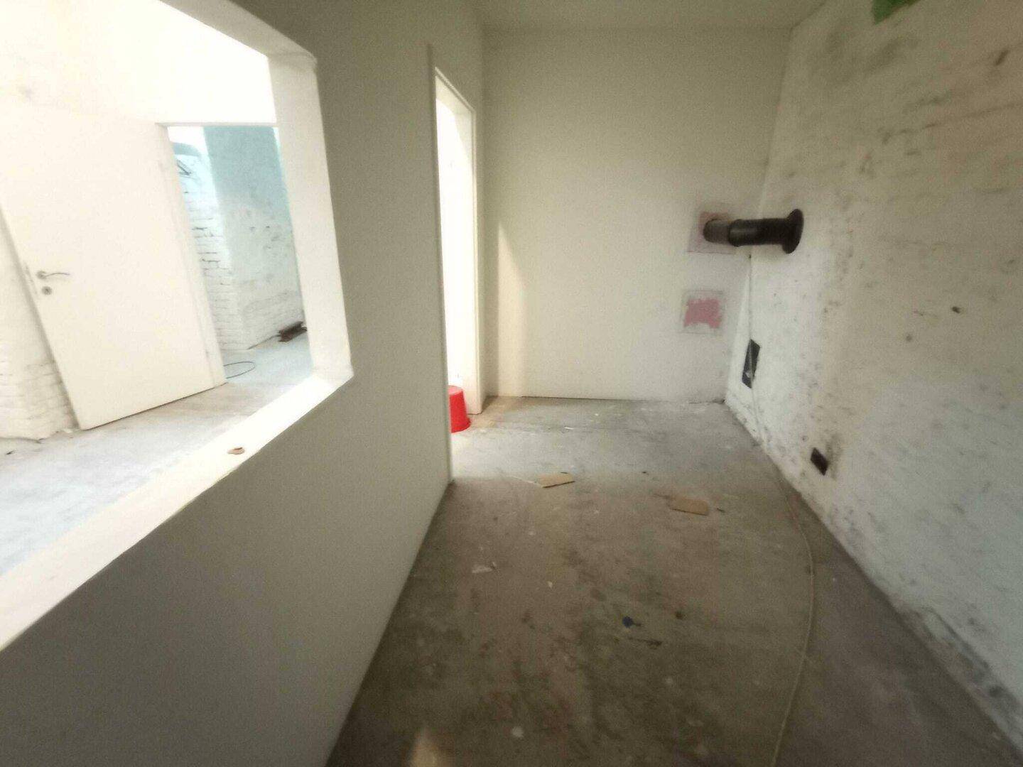 Kellerraum mit Betonboden, einer Wandöffnung und sichtbaren Installationen an der Wand, die auf Umbauarbeiten warten.