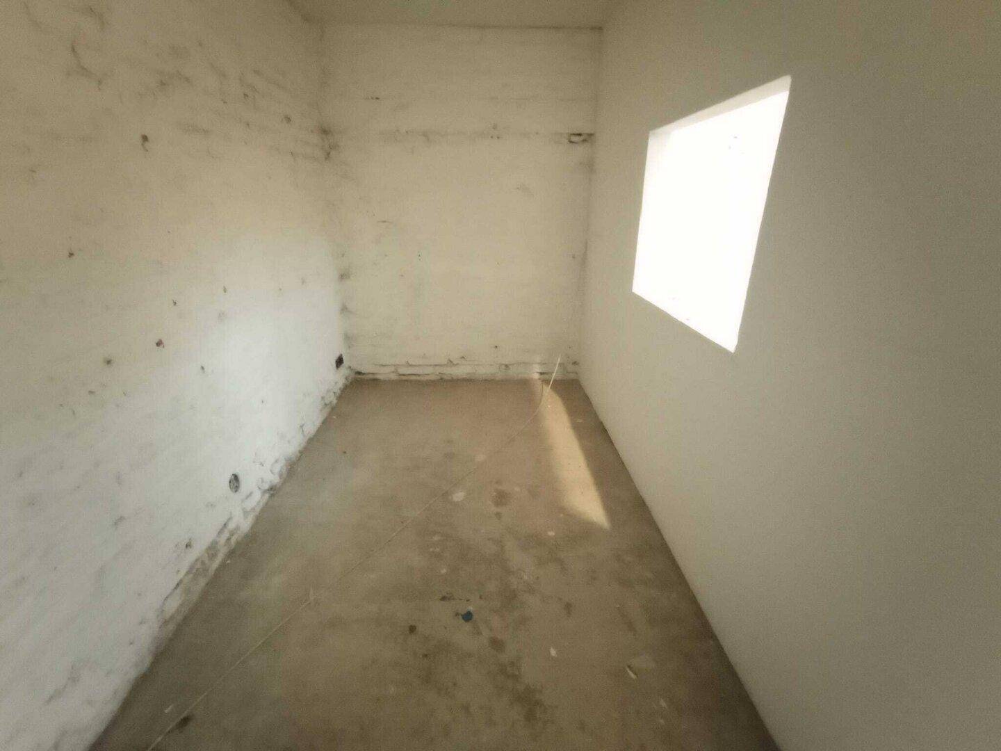 Langer, schmaler Kellerraum mit Betonboden und einer Fensteröffnung, die natürliches Licht hereinlässt.