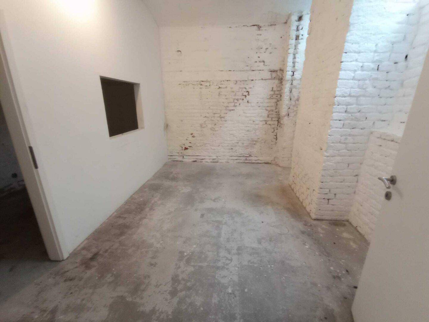 Kellerraum mit unverputzten Ziegelwänden und einem Durchbruch in der Wand, der auf weitere Arbeiten hinweist.