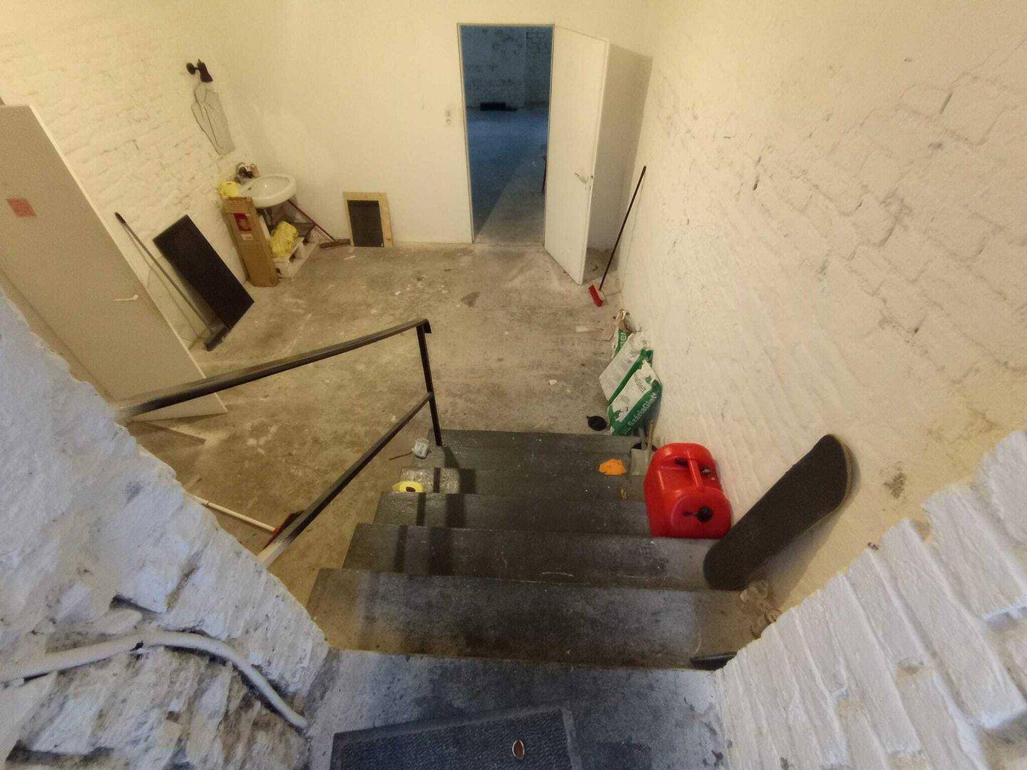 Blick in einen Kellerraum mit Treppe, unverputzten Wänden und verschiedenen Gegenständen, der Renovierung bedarf.