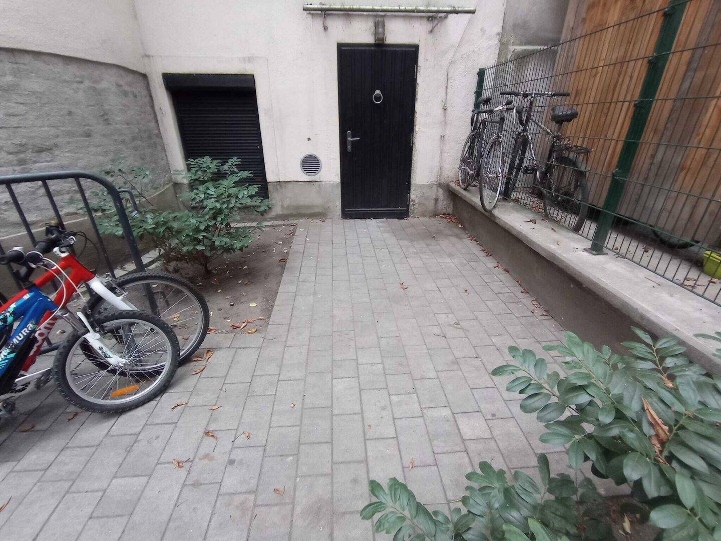 Gepflasterter Innenhof mit Fahrradständern und einer dunklen Eingangstür, die zu einem Gebäude führt.
