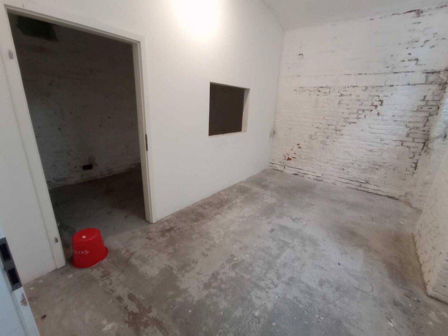 Kellerraum mit Betonboden, einer Öffnung in der Wand und unverputzten Ziegelwänden, die auf Renovierungsbedarf hindeuten.