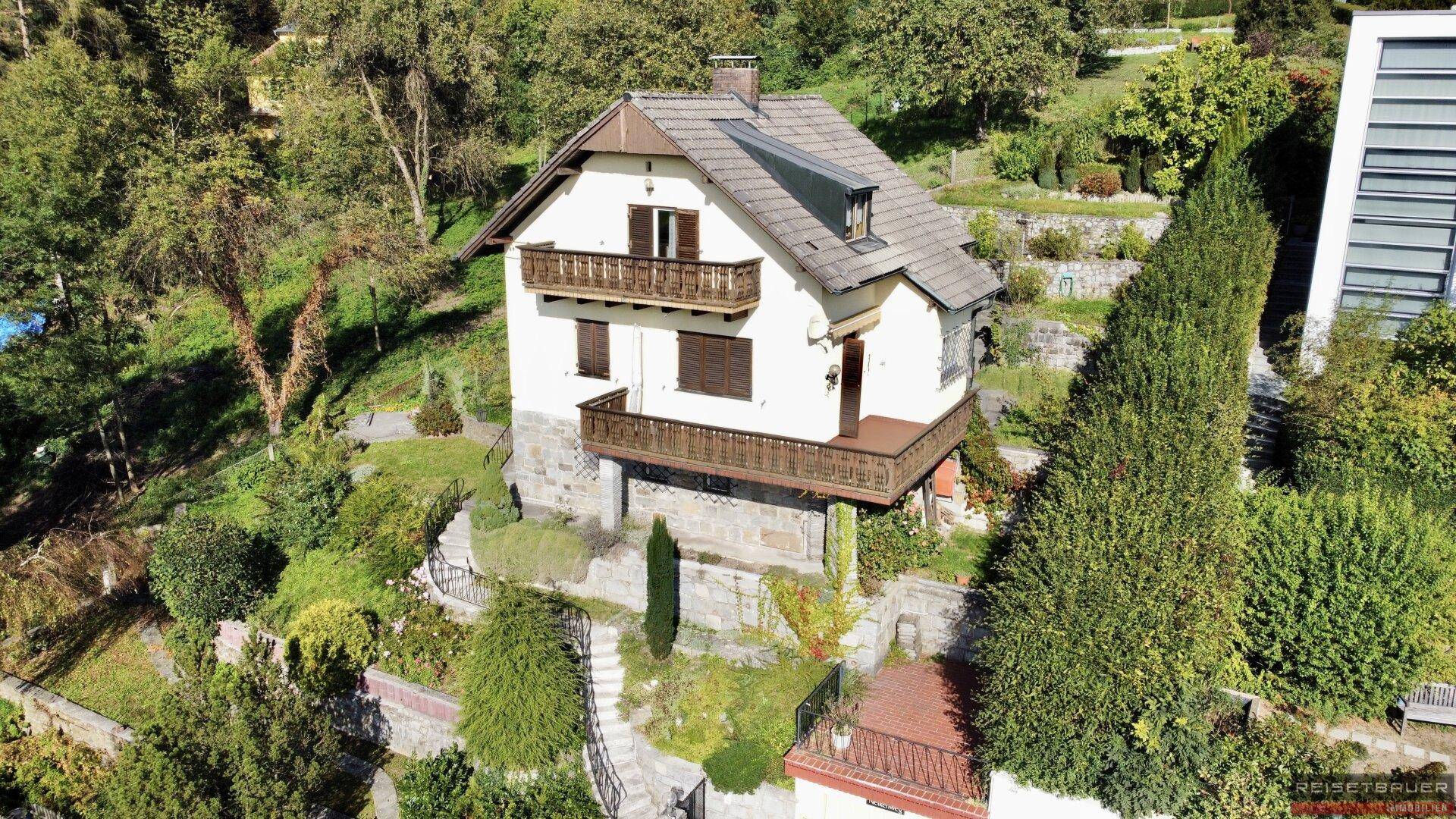 Traditionelles Haus mit mehreren Holzbalkonen und Satteldach, umgeben von üppiger Vegetation in Hanglage.