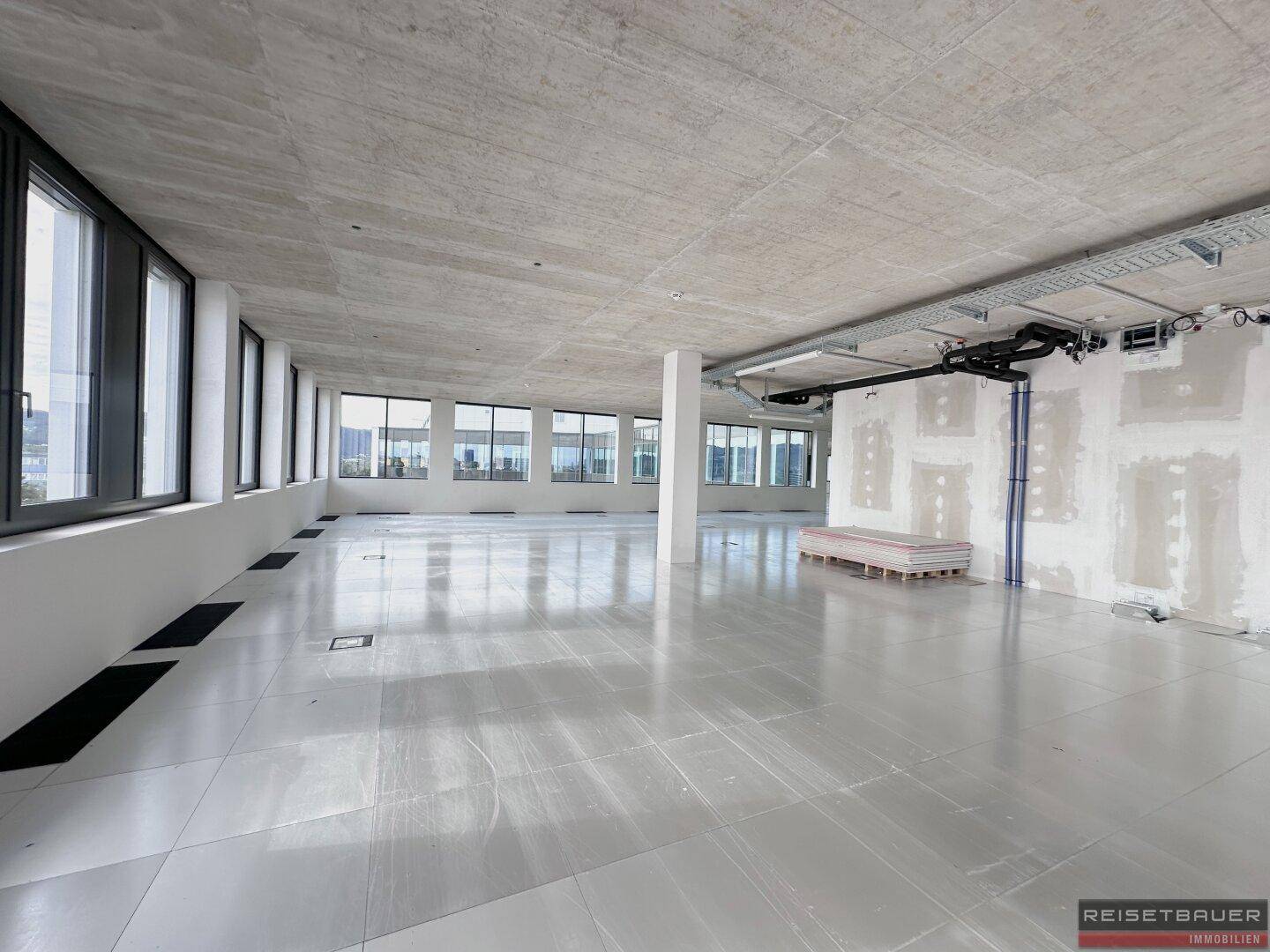 Geräumiger Büroraum im Rohbau mit unverputzten Wänden und sichtbaren Installationen, bereit für den Ausbau.