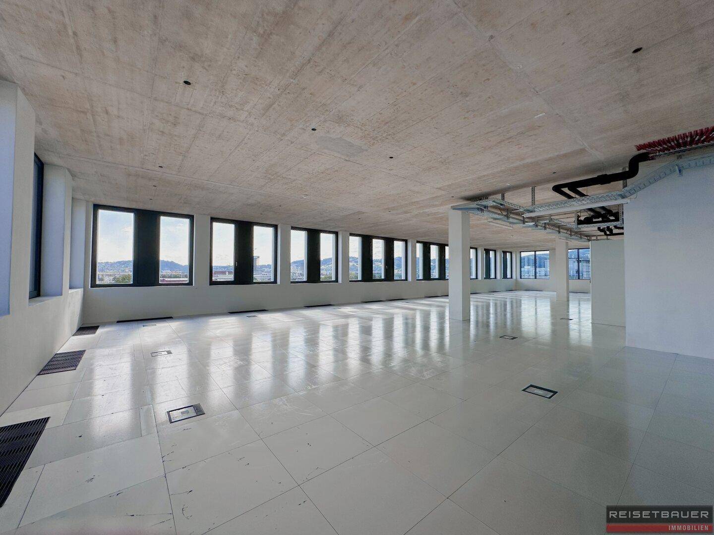 Langer, heller Bürogang mit vielen Fenstern und Blick auf die Umgebung, ideal für ein modernes Arbeitsumfeld.
