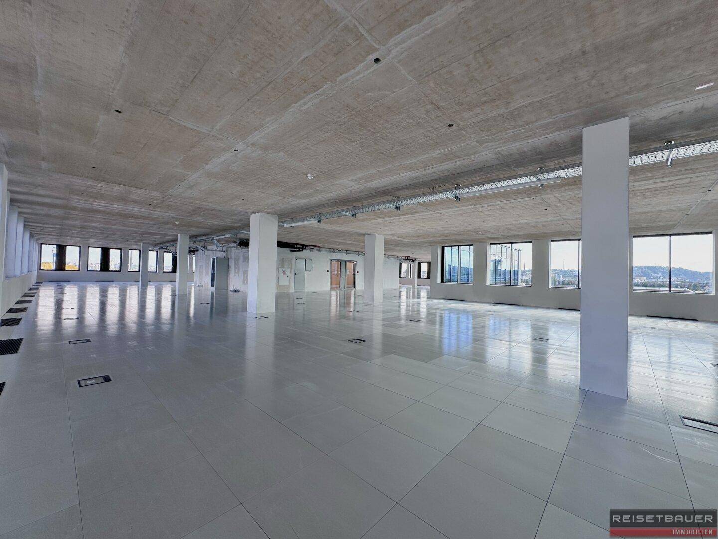 Weitläufiger Bürobereich mit Sichtbetondecke, großen Fenstern und Säulen, bereit für den Innenausbau.